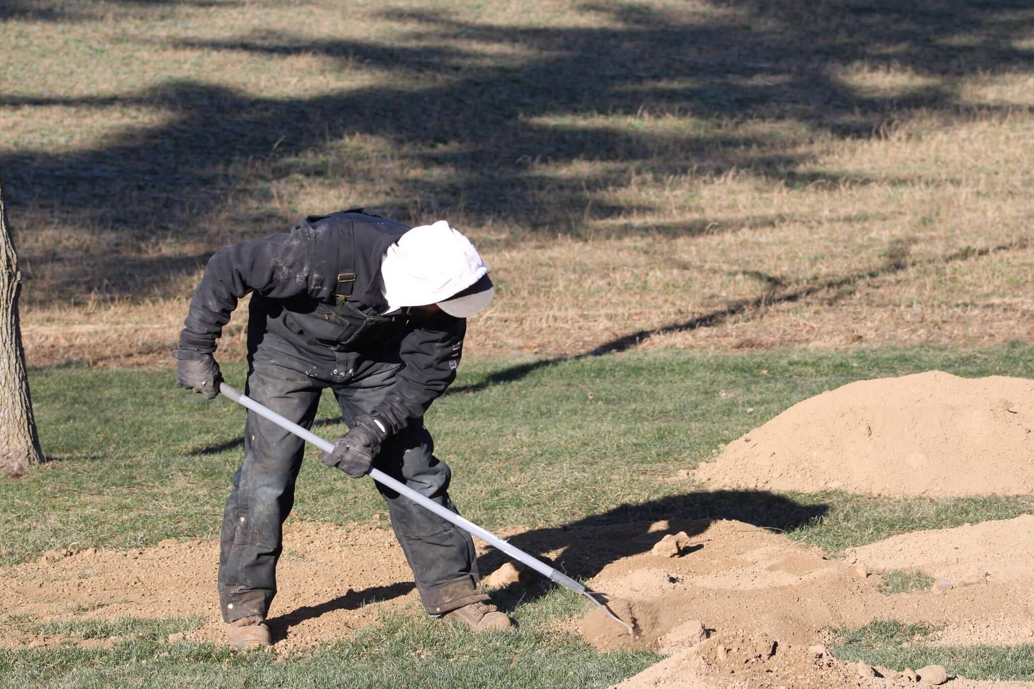 Muthler Landscaper know how to landscape a sloped backyard by leveling soil with a rake during a backyard project